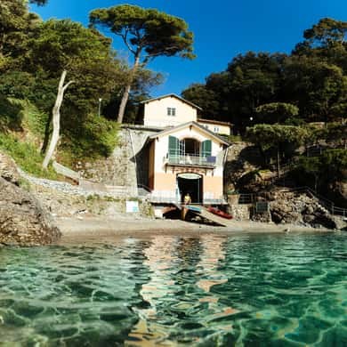 A small house on the rocks above clear green water