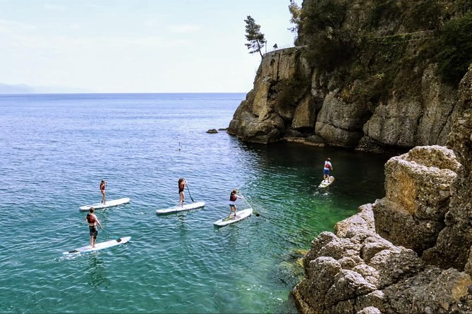 Paddleboarders crossing clear water below a rocky cliff