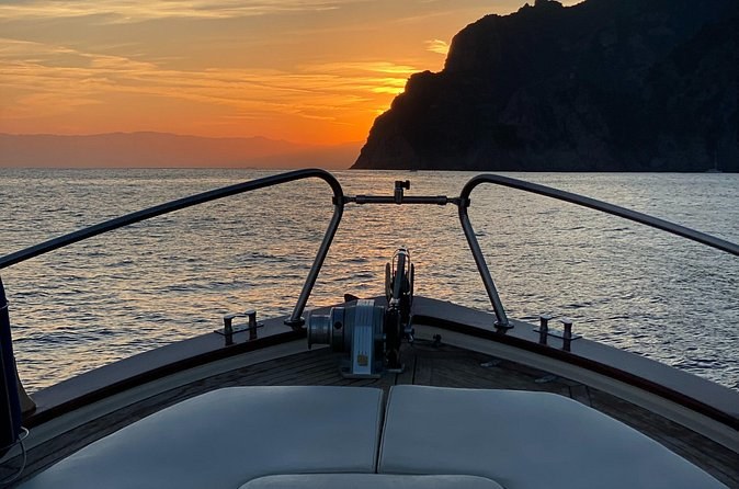 The sun setting behind a headland, seen over the bow of a boat