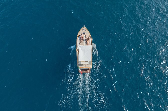 A wooden boat leaving a wake on deep blue water, from above